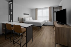 A hotel room with a bed, a desk with two chairs, a television, and a window with curtains.