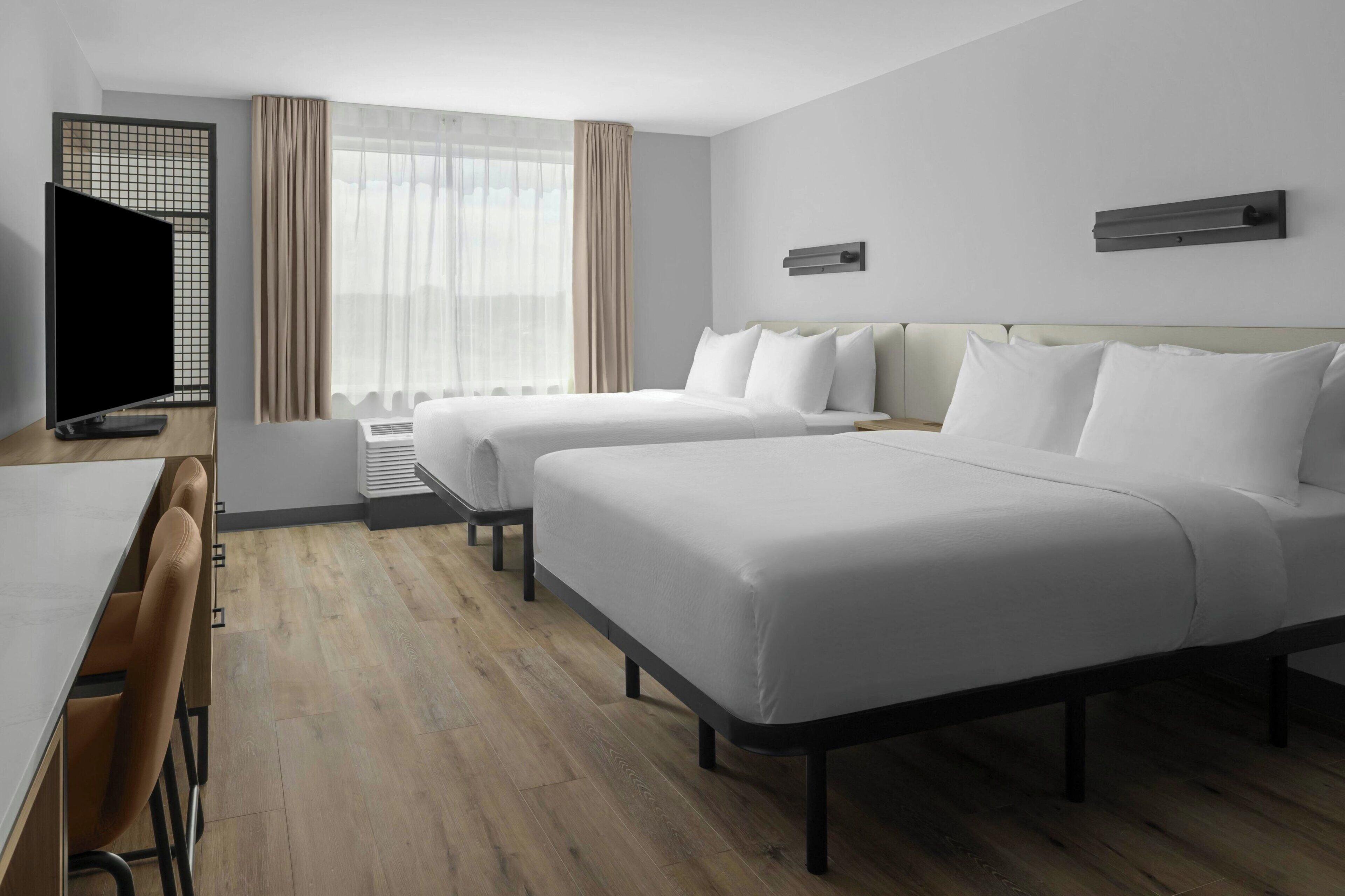 Habitación de hotel con dos camas, un escritorio, un televisor y una ventana con cortinas.