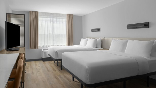 Habitación de hotel con dos camas, un escritorio, un televisor y una ventana con cortinas.