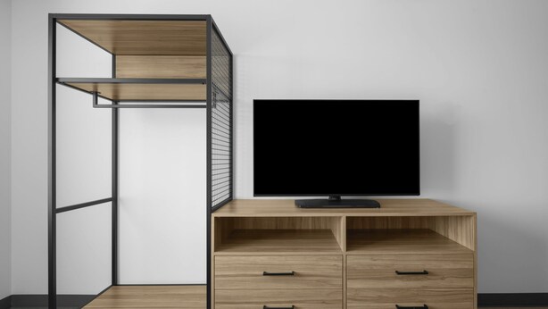 Habitació amb televisió sobre un escriptori de fusta, una prestatgeria metàl·lica i una televisió penjada a la paret.