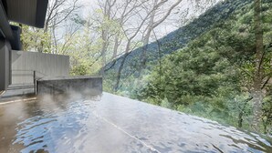 Un edificio moderno con techo plano, una escalera de piedra y vistas a una ladera boscosa.