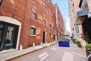 Eine schmale Stadtstraße mit roten Backsteingebäuden, einem blauen Blumenkasten und blauem Himmel.