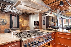 A kitchen with a large gas stove, wooden cabinets, and a brick wall. - Backstage Jam - 2 Units - Walk to Broadway (Nashville)
