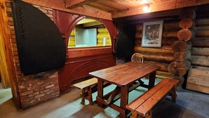 A rustic wooden interior with a wooden table and benches, a brick wall, and a wooden ceiling. - Boiler Room - Cozy log cabin at Haliburton Forest. (Dysart and Others)