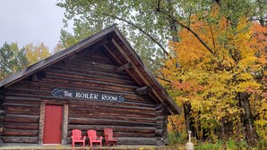 A log cabin with a red door and a sign reading 'The Boiler Room' with a 'Have Fun' slogan. - Boiler Room - Cozy log cabin at Haliburton Forest. (Dysart and Others)