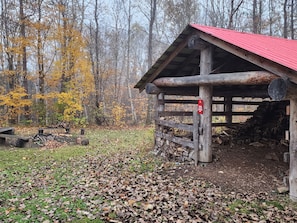 A rustic cabin with a red roof, surrounded by a forest with autumn-colored trees.