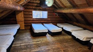 A cabin with four beds arranged in a row, wooden walls, a small window, and a ceiling fan. - Boiler Room - Cozy log cabin at Haliburton Forest. (Dysart and Others)