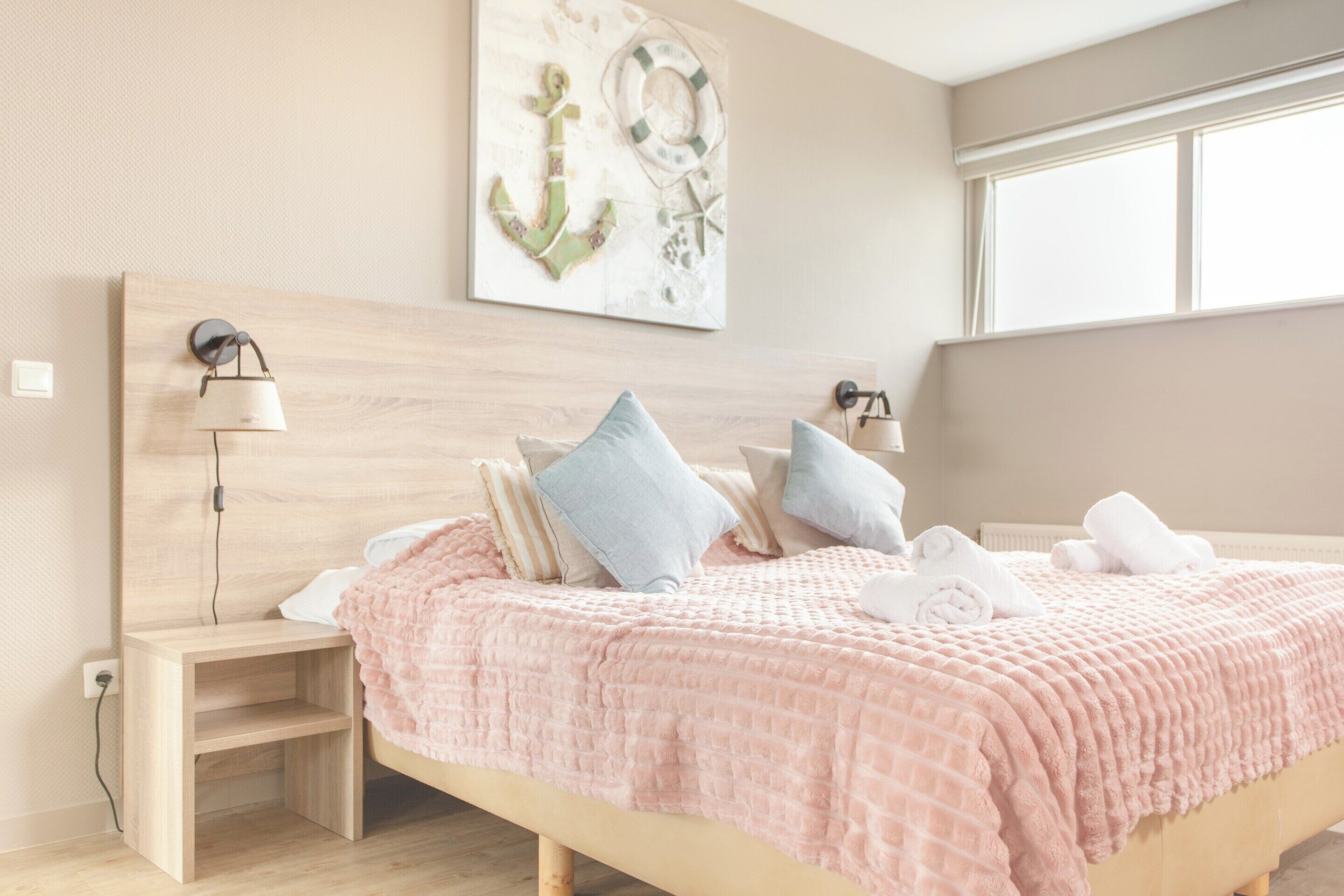 Una habitación de hotel con cama, mesitas de noche, una obra de arte en la pared y un ventanal.