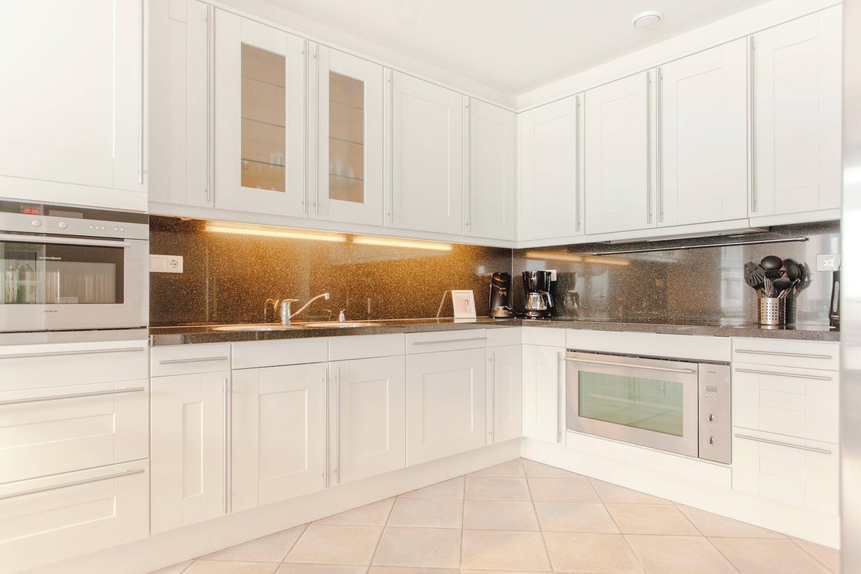 Una cocina moderna con armarios blancos, horno de acero inoxidable, cafetera y pileta.