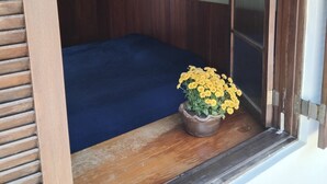 A room with a wooden-framed window, a blue bed, and a potted plant with yellow flowers.