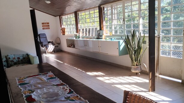A room with a long table covered by a tablecloth, a sofa, and a window with a view of greenery.