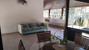 A living room with a sofa, a glass-top table, wicker chairs, and a view of the outside.