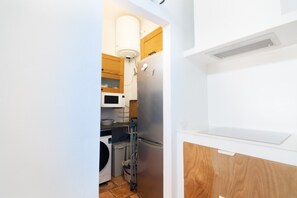 Cocina compacta con refrigerador de acero inoxidable, microondas y armarios de madera.