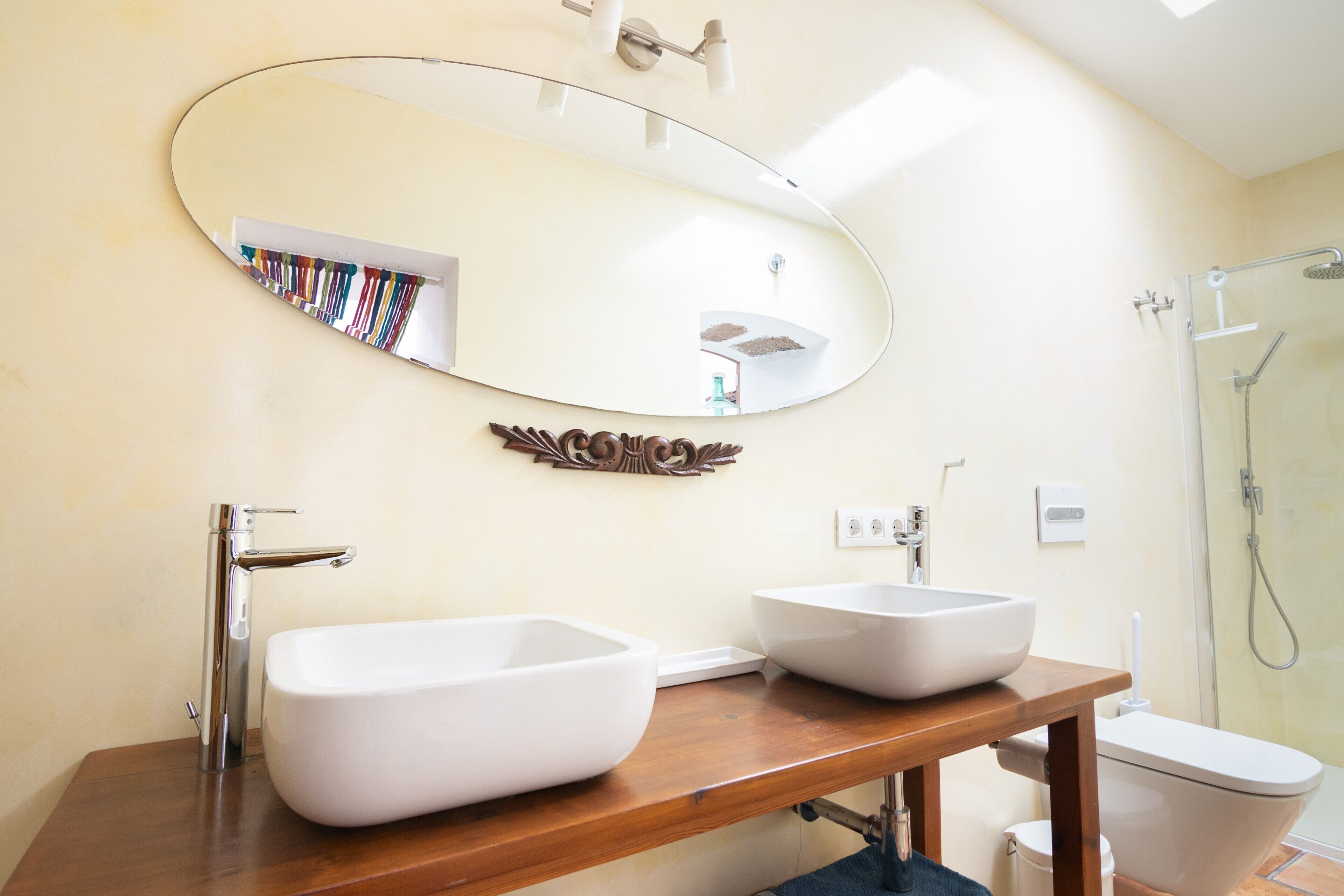 Une salle de bain avec deux lavabos blancs, un meuble-lavabo en bois, un grand miroir et un espace douche.