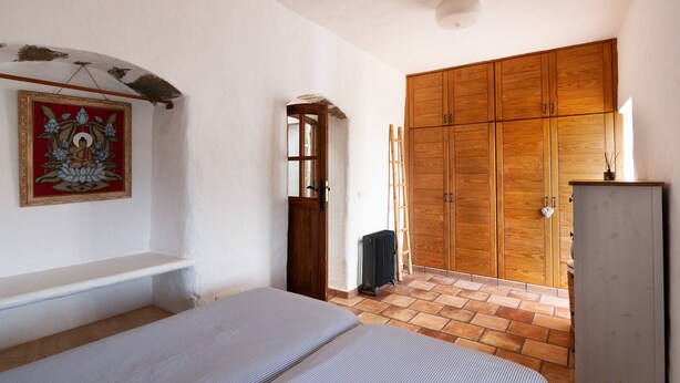 Una stanza con un letto, un armadio in legno, un termosifone e una porta che dà su un'altra stanza.