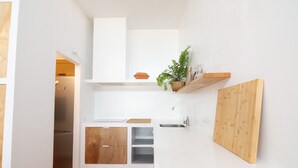 Una cucina compatta con mobili bianchi, un piano di lavoro in legno, un lavello incassato e una piccola pianta su uno scaffale.