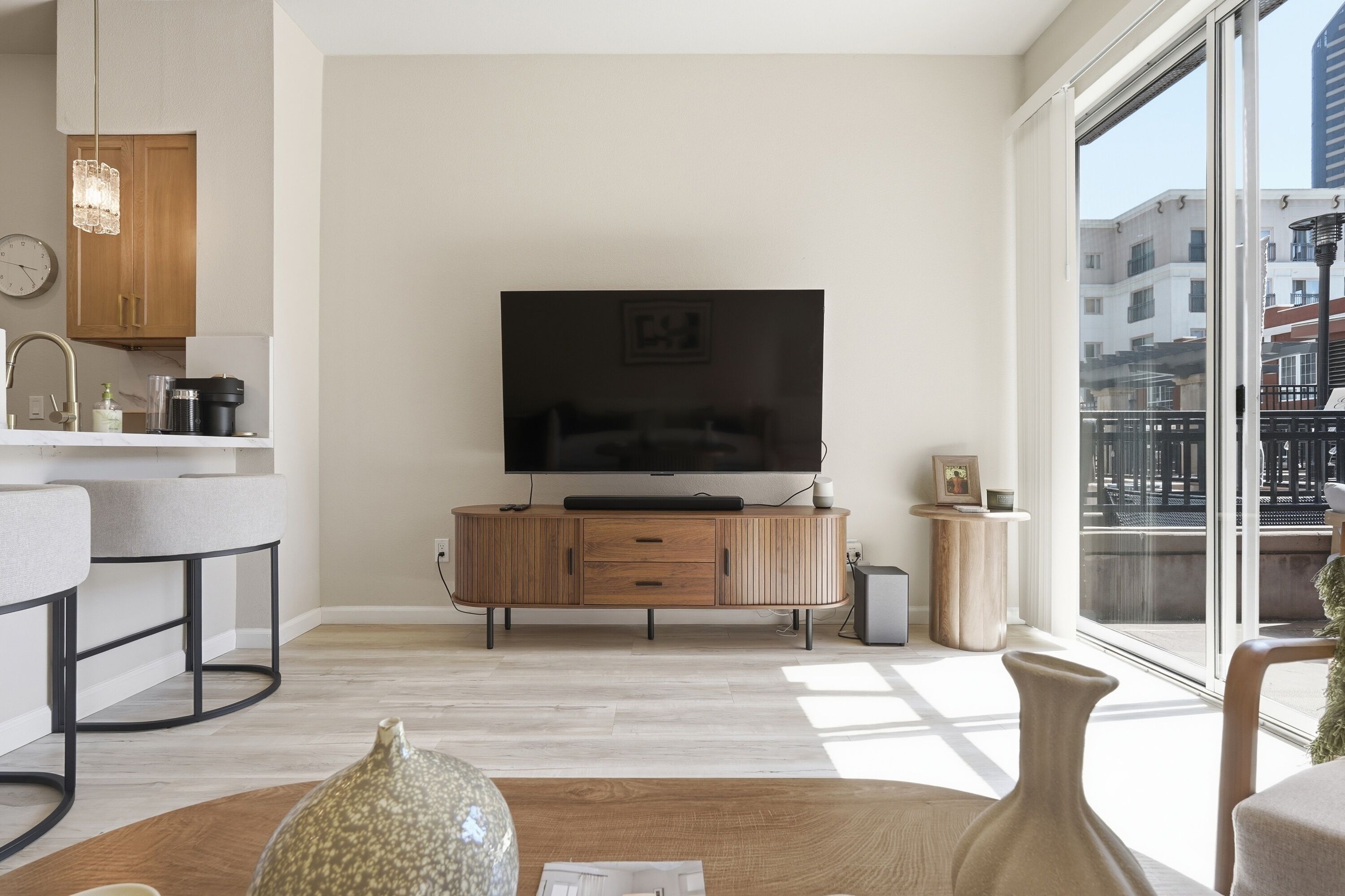 Een moderne woonkamer met een flatscreen televisie, een houten kast en een groot raam met uitzicht op de stad.