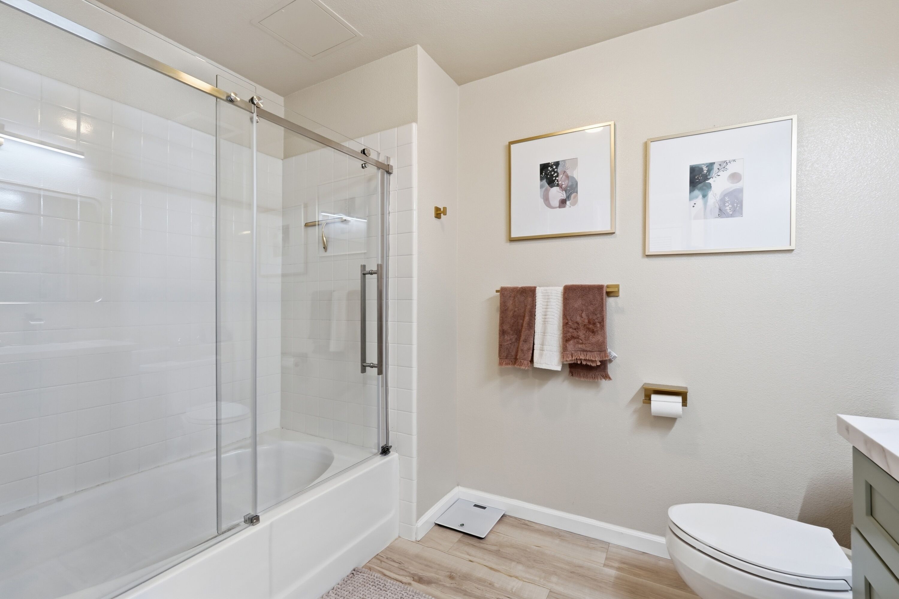 Une salle de bain moderne avec une douche à parois de verre, des toilettes et deux tableaux encadrés au mur.
