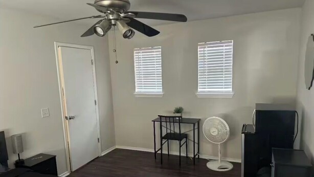 A bedroom with a bed, a ceiling fan, a desk, a chair, a small table, a fan, and a dresser.