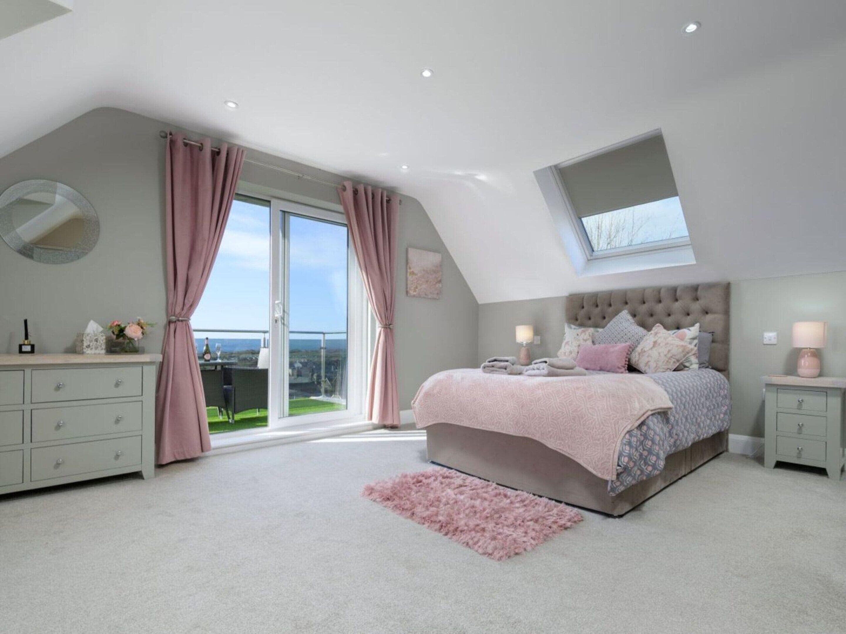 A bedroom with a large bed, a dresser, a nightstand, a window with curtains, and a skylight.
