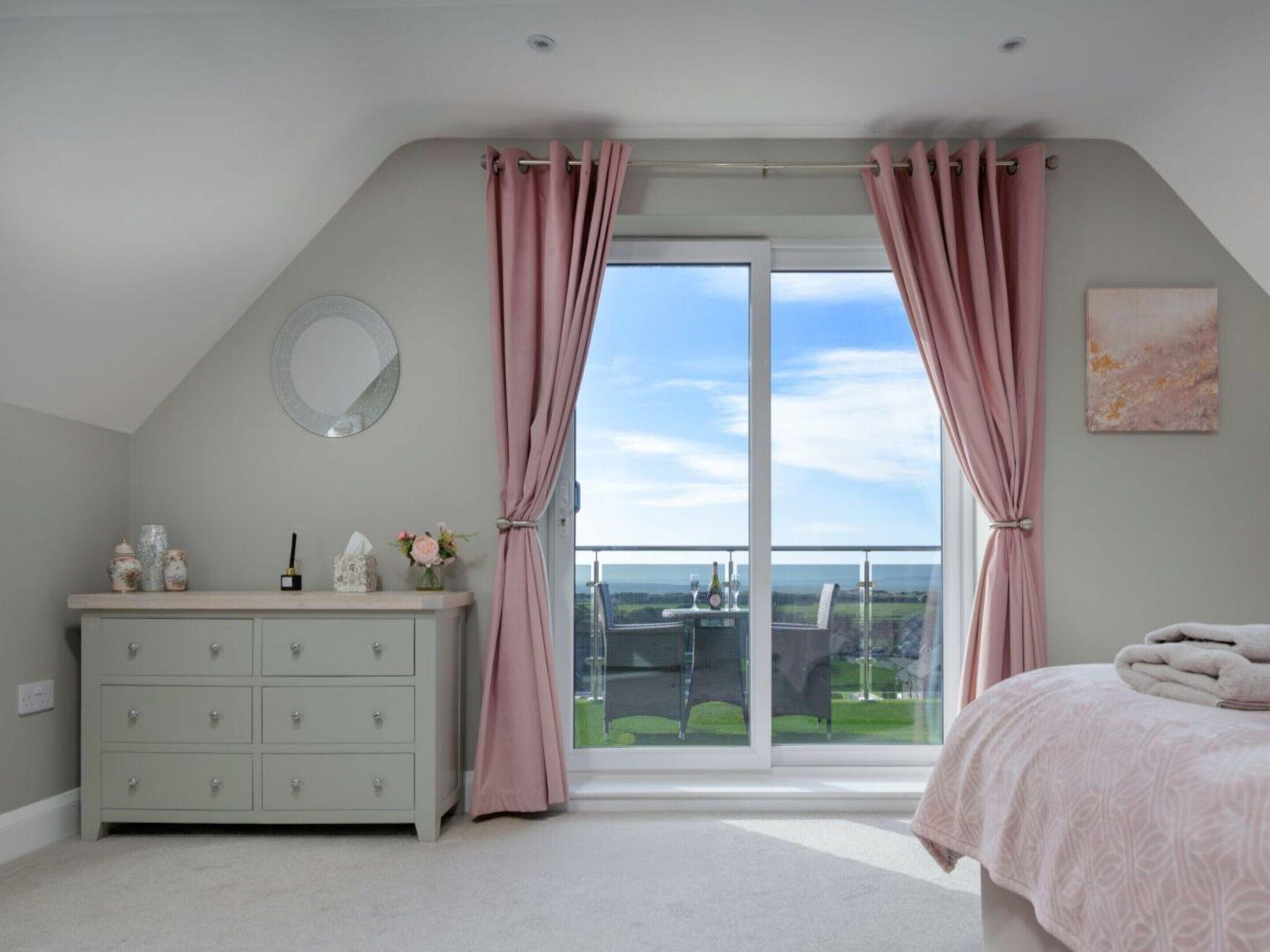 Une chambre avec une grande fenêtre, une commode, un lit et une vue sur l’extérieur.
