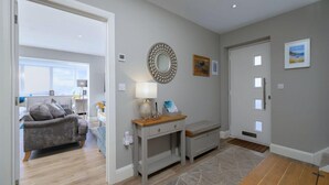 A modern interior with a grey sofa, a wooden bench, a mirror, and a door with windows. - Luxury Whitby Townhouse for 10 (Dyffryn Ardudwy)