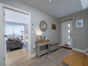 A modern interior with a grey sofa, a wooden bench, a mirror, and a door with windows. - Luxury Whitby Townhouse for 10 (Dyffryn Ardudwy)