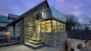 A modern house with a stone exterior, a glass-enclosed porch, and a paved patio area. - Luxury Whitby Townhouse for 10 (Dyffryn Ardudwy)