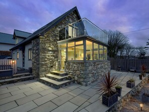 A modern house with a stone exterior, a glass-enclosed porch, and a paved patio area. - Luxury Whitby Townhouse for 10 (Dyffryn Ardudwy)