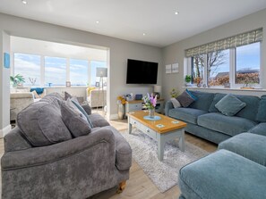 Ein modernes Wohnzimmer mit einem grauen Sofa, einem blauen Sofa, einem Holztisch und einem Flachbildfernseher.