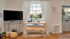 Una sala de estar moderna con un televisor de pantalla plana, una mesa de comedor con un banco, un radiador y una ventana con cortinas.