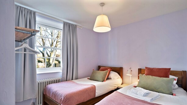 Un dormitorio con dos camas individuales, un radiador, una ventana con cortinas y una lámpara colgante.