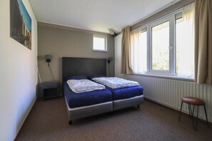 A single-bed room with a window, a nightstand, a chair, and a painting on the wall. - Compact Waterfront Wellness Bungalow (Makkum)