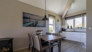 A modern kitchen with a dining area, featuring a large wooden table, chairs, a hanging light fixture, and a painting on the wall. - Compact Waterfront Wellness Bungalow (Makkum)