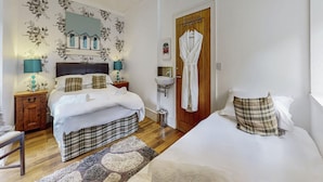 Una camera d'albergo con un letto, comodini, uno specchio, una porta in legno e un bagno con un lavandino.