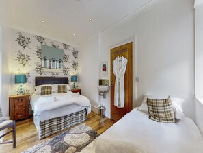 Habitación de hotel con cama, mesitas de noche, un espejo, puerta de madera y baño con lavamanos.