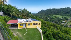 A yellow building with a red roof, solar panels, and a fenced yard. - Hilltop Getaway With Huge Terrace (Fajardo)