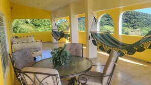 A room with a round glass table, two chairs, a sofa, and two hammocks. - Hilltop Getaway With Huge Terrace (Fajardo)