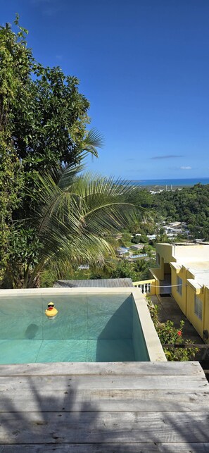 A swimming pool with a view of a coastal landscape, surrounded by lush greenery and a clear blue sky. - Hilltop Getaway With Huge Terrace (Fajardo)