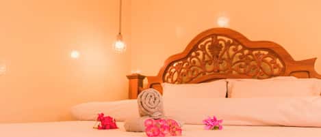 A neatly made bed with a wooden headboard, a rolled towel, and pink flowers on the bed.