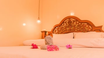 Una cama bien tendida con cabecera de madera, una toalla enrollada y flores rosadas sobre la cama.