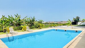 A rectangular swimming pool with a tiled edge, surrounded by a wooden deck. - Stylish East Legon 1BR | Pool & Gym (Accra)