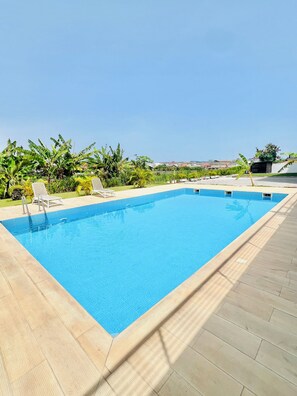 Piscina retangular com borda revestida em azulejo, rodeada por um deck de madeira.