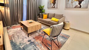 A modern living room with a sofa, coffee table, and a chair. There are two paintings on the wall and a plant in the corner. - Stylish East Legon 1BR | Pool & Gym (Accra)