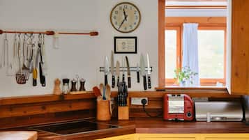 Una cocina con armarios de madera, un reloj, diferentes utensilios y un electrodoméstico rojo sobre la encimera.