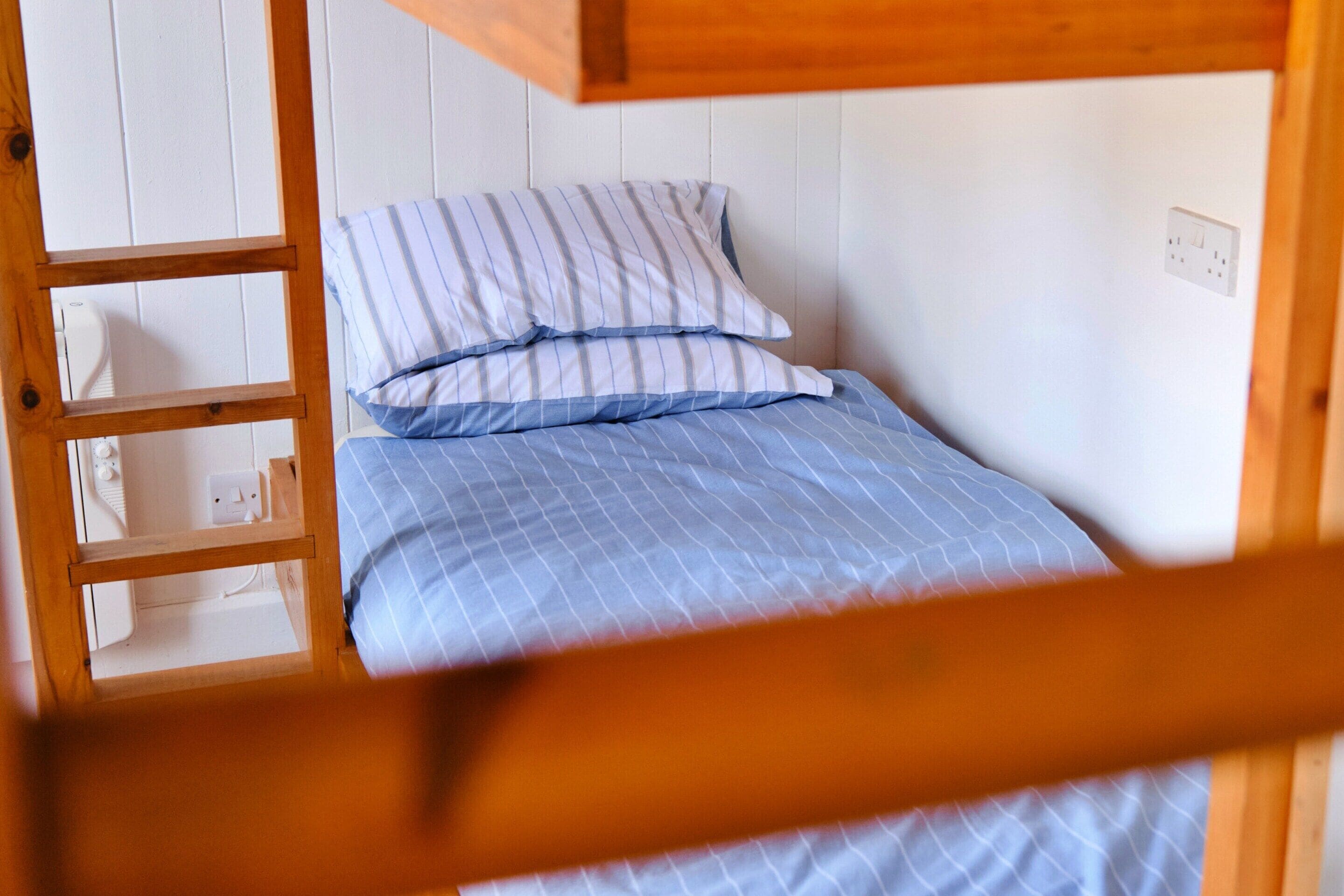 Una cama litera con colcha azul a cuadros y almohadas a rayas.