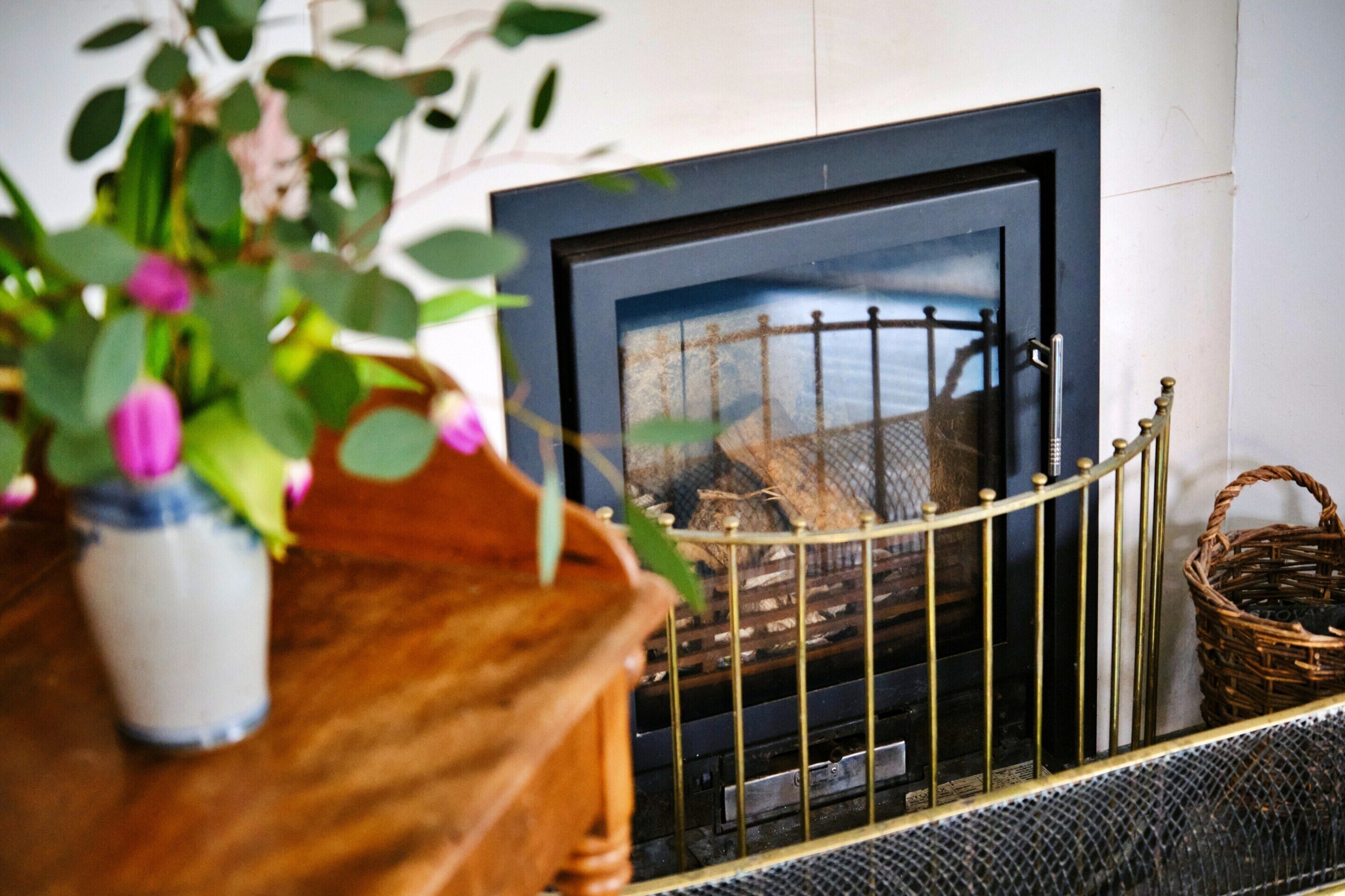 Una chimenea con una protección metálica, repisa de madera y una cesta de mimbre.