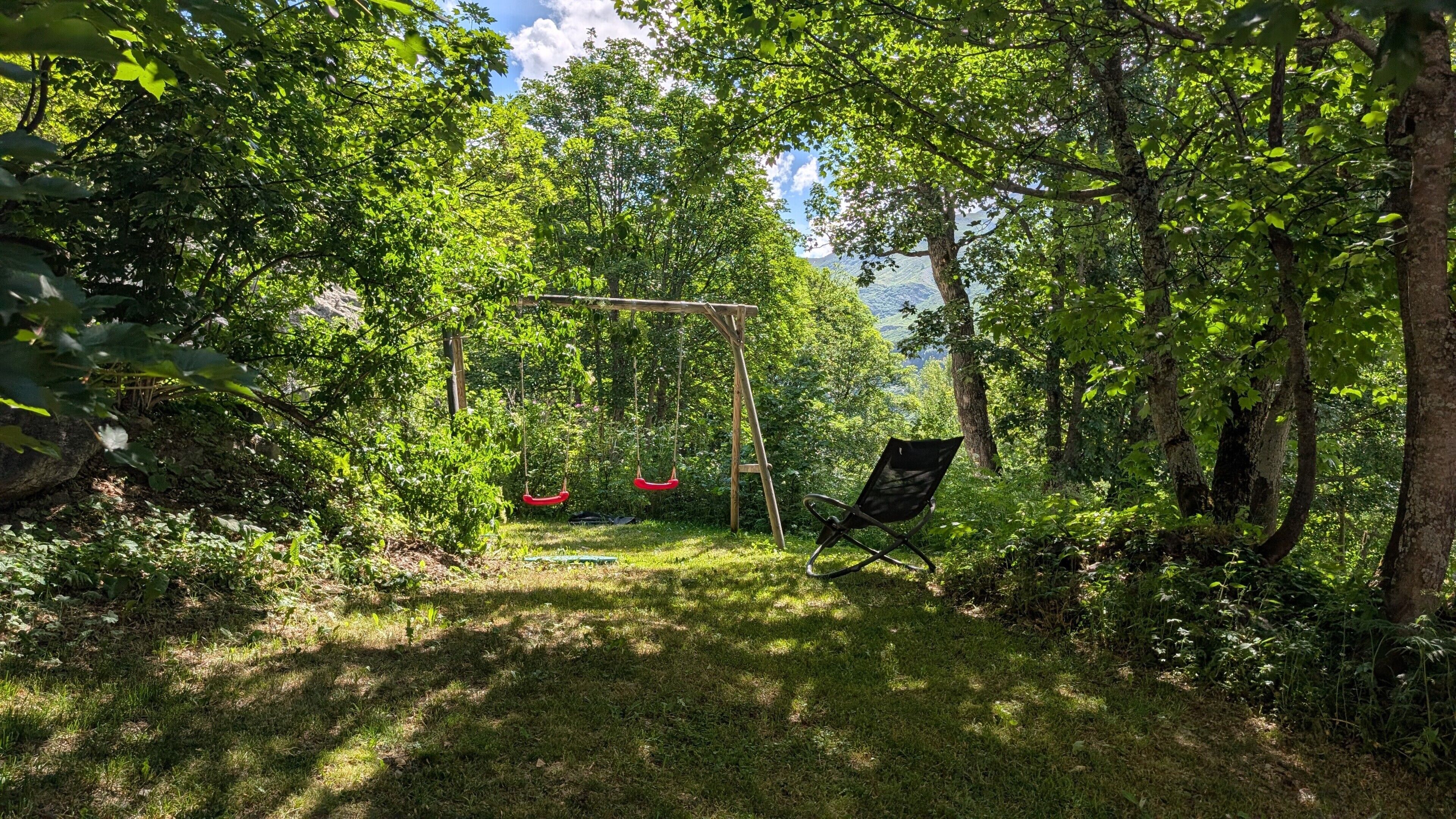 A garden with a swing set and a chair, surrounded by trees and greenery.