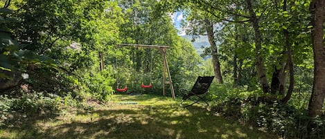 A garden with a swing set and a chair, surrounded by trees and greenery.