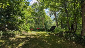 Ein Garten mit Schaukel und Stuhl, umgeben von Bäumen und viel Grün.